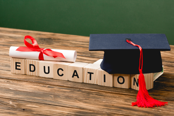 wooden blocks with letters, academic cap and diploma on wooden surface isolated on green - Photo, Image