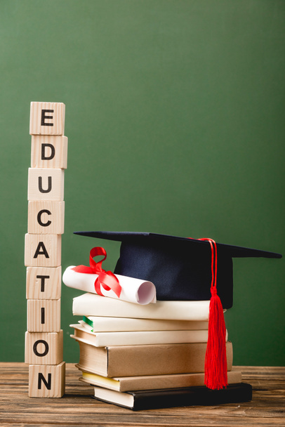 wooden blocks with letters, books, academic cap and diploma on wooden surface isolated on green - Photo, Image