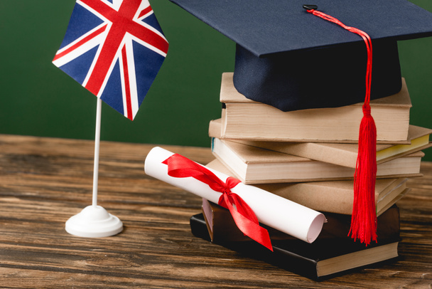 Books, academic cap, diploma and british flag on wooden surface isolated on green - 写真・画像