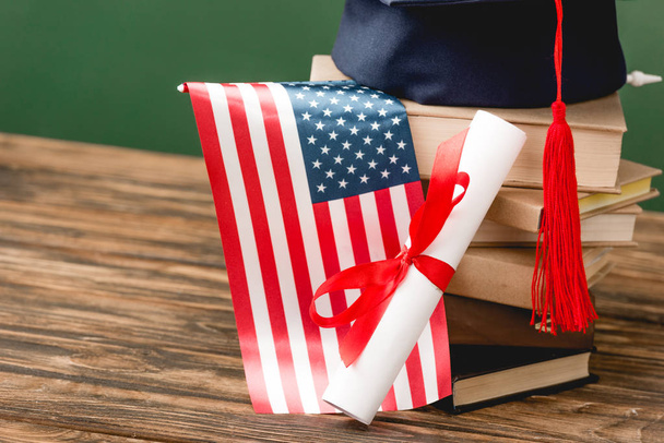 books, academic cap, diploma and american flag on wooden surface isolated on green - Photo, Image