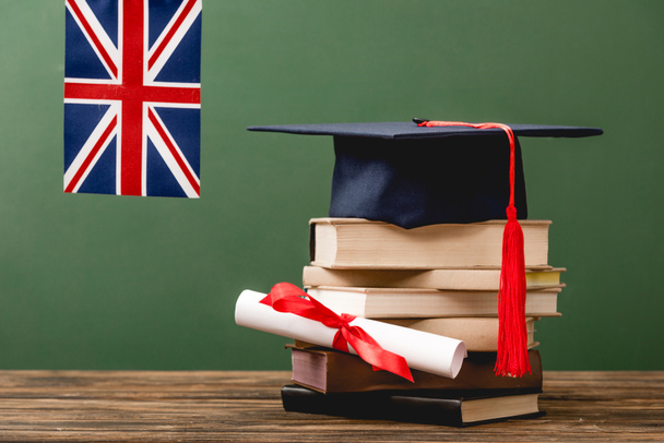 Books, academic cap, diploma and british flag on wooden surface isolated on green - Foto, Imagen