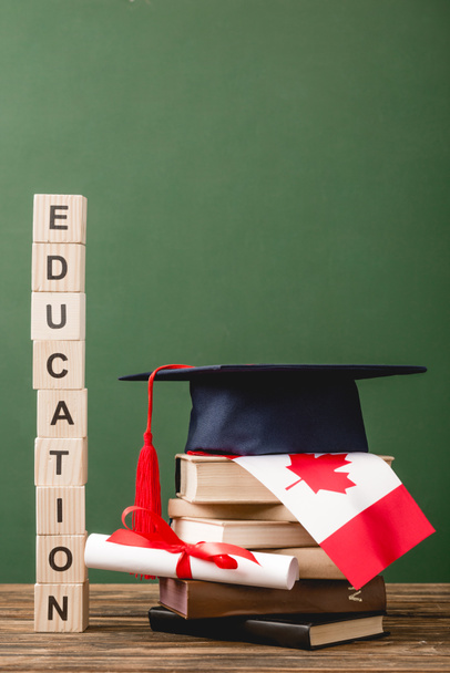 wooden blocks with letters, academic cap, books, diploma and canadian flag on wooden surface isolated on green - Photo, Image