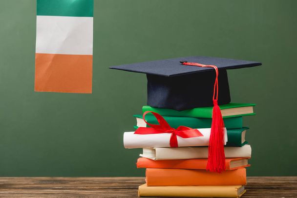books, diploma, academic cap and irish flag on wooden surface isolated on green - Фото, зображення