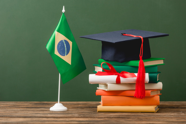 libros, gorra académica, diploma y bandera brasileña sobre superficie de madera aislada en verde
 - Foto, Imagen