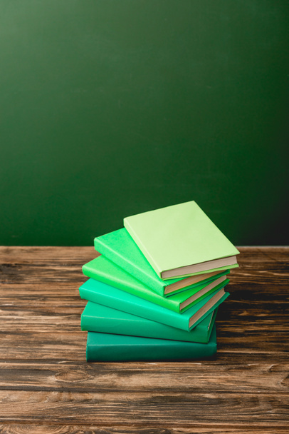 stack of colorful books on wooden surface isolated on green - Photo, Image