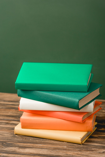 stack of colorful books on wooden surface isolated on green - Fotó, kép