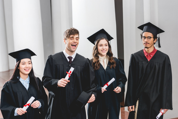 lachende groep studenten in afstuderen jassen Holding diploma's  - Foto, afbeelding