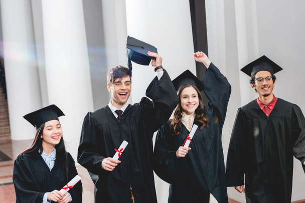 happy group on students gesturing and celebrating graduation while holding diplomas  - Φωτογραφία, εικόνα
