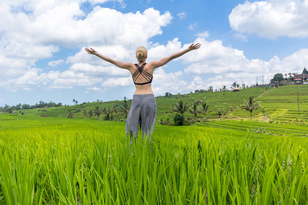 Mujer deportiva sana relajada, brazos levantados al cielo, disfrutando de la naturaleza pura en hermosos campos de arroz verde en Bali
. - Foto, imagen