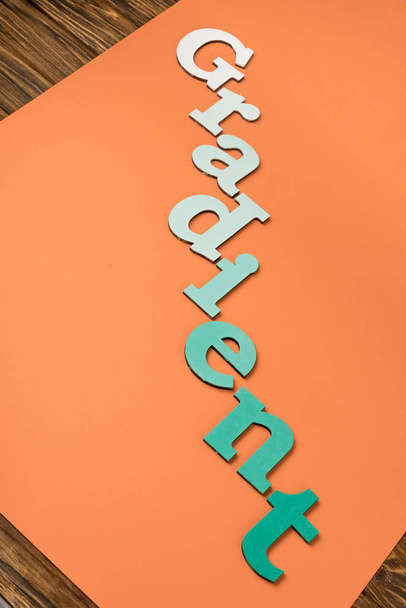 gradiënt woord gemaakt van groene letters op helder oranje papier  - Foto, afbeelding