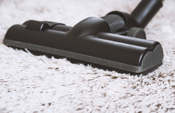 Close up of the head of a modern vacuum cleaner being used while vacuuming a thick pile white carpet.still life dark tone. - Photo, Image