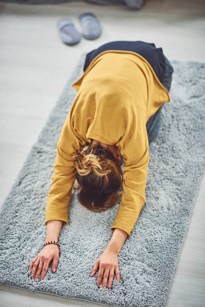 Brunette doing Extended Child's yoga posture on the rug in bedroom. - Foto, Imagen