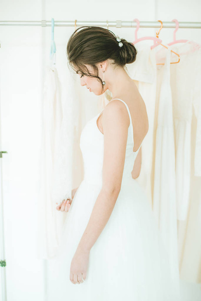 Beautiful young bride in a white dress in the salon on the background of other wedding dresses - Fotografie, Obrázek