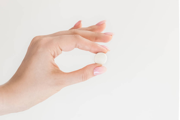 white round pill in hand, medicine in female fingers not white background, isolate, pills, one pill - Фото, изображение