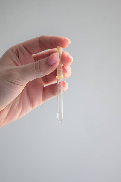 medical ordinary pipette in a woman's hand, clear liquid, beautiful female fingers, a drop on the pipette - Foto, Imagem