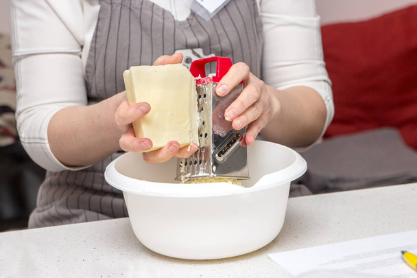 Detail of female hands grate cheese. Women prepare cheese in the kitchen for pizza or pie. Baking concept - Photo, Image