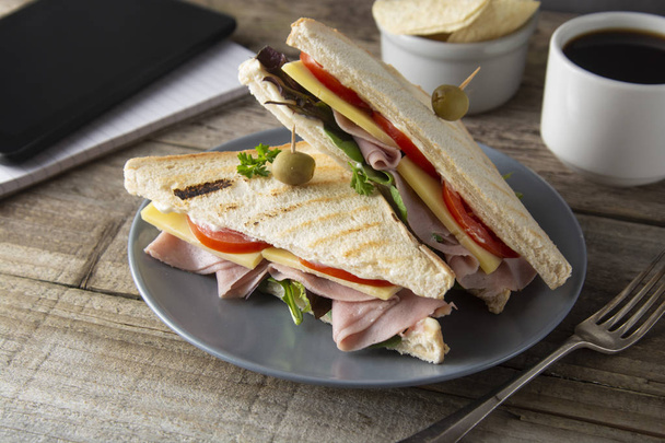Unhealthy eatting at work place. Triangle, club sandwich with ham and vegetables. Tablet, gadget screen and notebook. Cup of coffee. Fast food. - Φωτογραφία, εικόνα