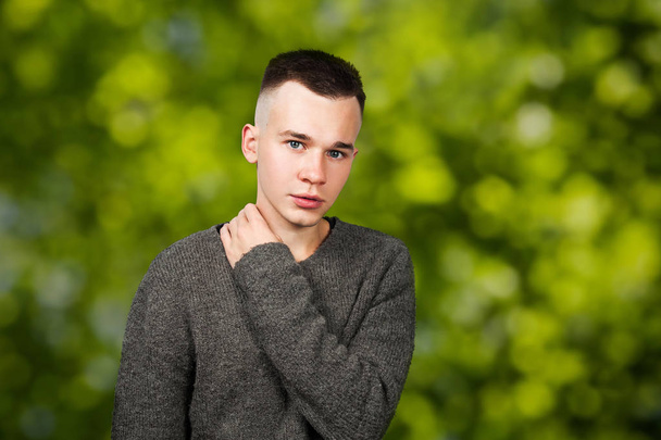 Portrait of white yong guy in gray sweater and short haircut, on green bokeh background - Фото, изображение