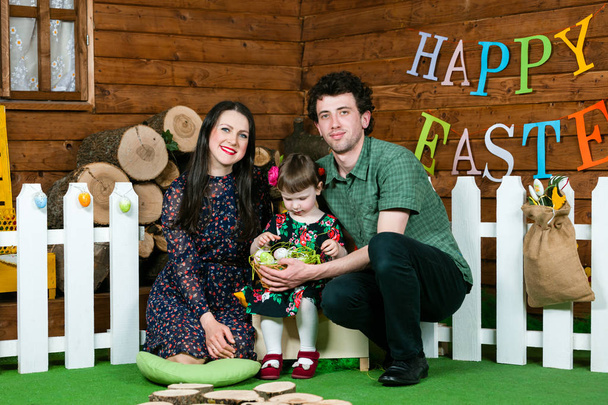 Vacaciones de Pascua. Los padres y la hija juegan con huevos de Pascua. En la pared la escritura Feliz Pascua
. - Foto, Imagen