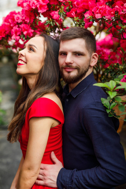 young beautiful couple girl in red dress man in blue shirt stand in garden with flowers - Foto, Bild