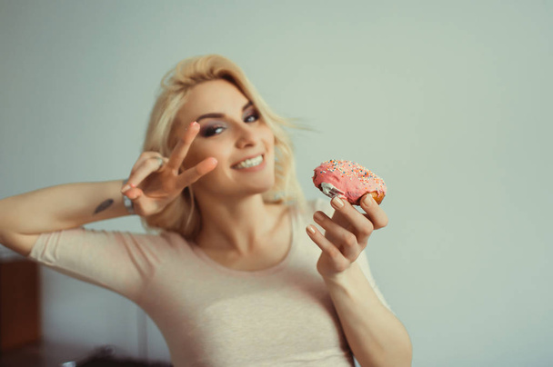 Lächelnde blonde Zwillinge mit Sonnenbrille essen Donuts und genießen mit geschlossenen Augen über rosa Hintergrund, schnellen Fuß, süße Torte, Pfannkuchen, Kuchen, Hipster-Porträt, bali - Foto, Bild