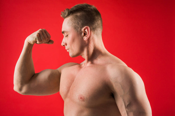handsome young man in athletic form on red background shows his muscles - Φωτογραφία, εικόνα