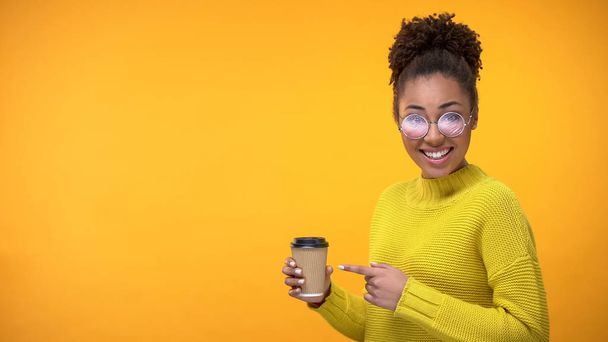 Elegante joven mujer apuntando a la taza de papel de café y la cámara sonriente, sorpresa
 - Foto, Imagen