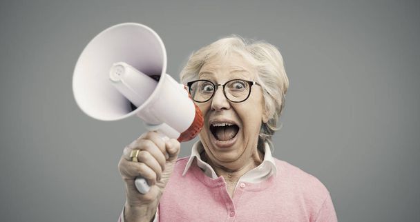 Cheerful senior lady shouting into a megaphone - Foto, Imagen