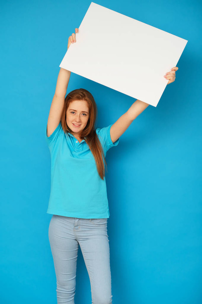 Ginger girl holding a whiteboard on blue background. - Fotoğraf, Görsel