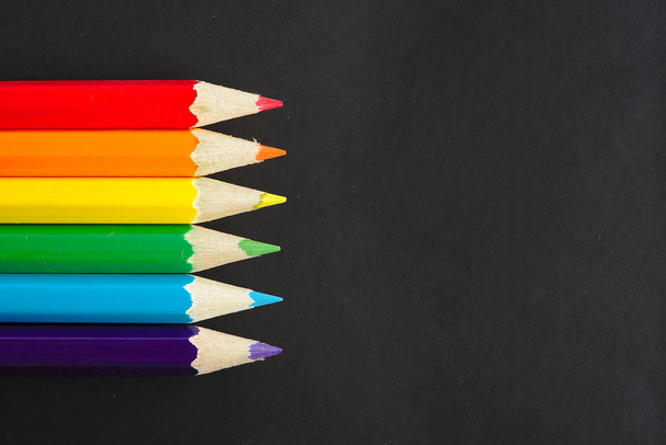 six rainbow colored pencils on a black sheet with space for text - Photo, Image