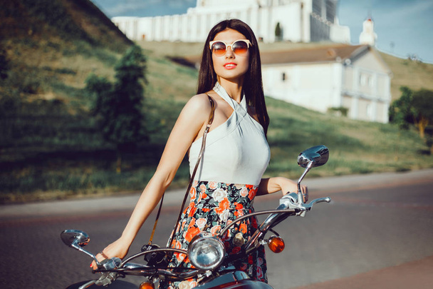 Mujer de belleza posando en la calle, hacer foto en la cámara vintage y posando cerca de la motocicleta, bicicleta, scooter, retrato hipster al aire libre
 - Foto, Imagen