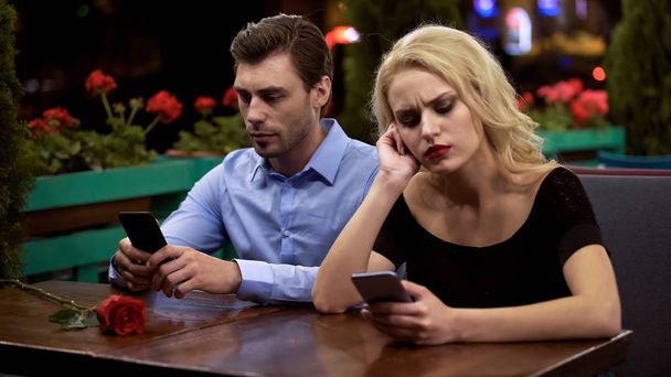 Two young people boring on date, using smartphones, problems in relationship - Photo, Image