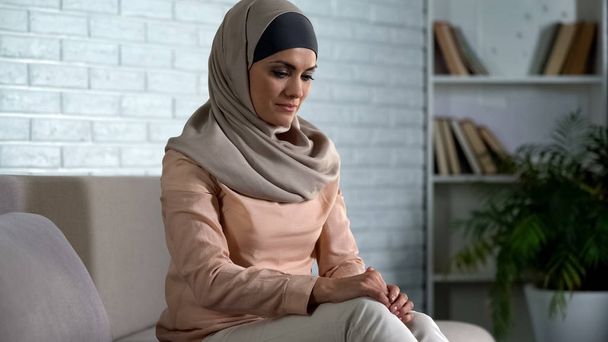 Shy muslim female sitting on sofa at home, waiting husband from work, marriage - Fotografie, Obrázek