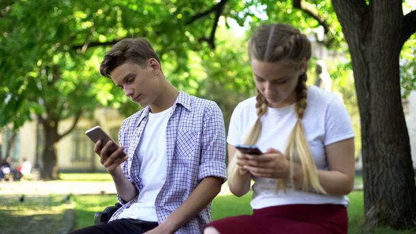 Indifferent teenagers scrolling smartphones in park, gadget addiction problem - Photo, image