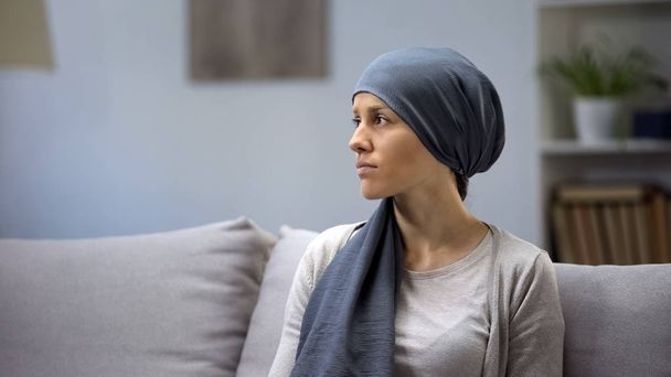 Upset young lady in headscarf lonely sitting on sofa in oncologic hospital - Фото, изображение