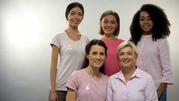 Група жінок в рожевих сорочках зі стрічками раку молочної залози дивиться в камеру
 - Фото, зображення