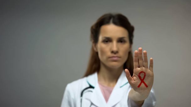 Young lady doctor showing red ribbon sign on hand, AIDS awareness campaign - Фото, зображення