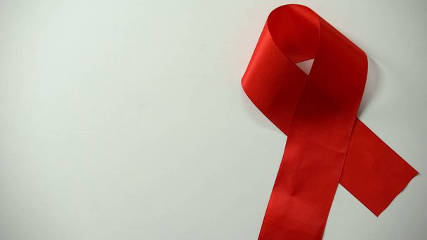 Κόκκινη κορδέλα βρίσκεται στο τραπέζι, AIDS ευαισθητοποίηση και πρόληψη, υγειονομική περίθαλψη, εκστρατεία - Φωτογραφία, εικόνα