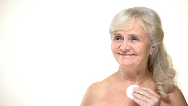 Mujer anciana alegre usando almohadilla para la limpieza de la piel, procedimientos de belleza, cosméticos
 - Foto, Imagen