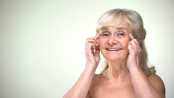 Ελκυστική γριά γυναίκα κάνει ασκήσεις προσώπου, αντιγηραντική πρόσοψη για τα μάτια - Φωτογραφία, εικόνα