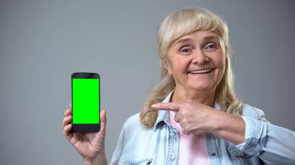 Smiling elderly woman showing smartphone with green screen, advertisement - Foto, afbeelding