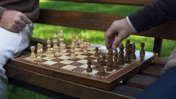 Grandfathers playing chess on bench, moving figures on board, game beginning - Fotó, kép