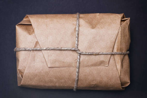 Craft wrapped package on black background. Parcel with hemp cord.  - Фото, изображение