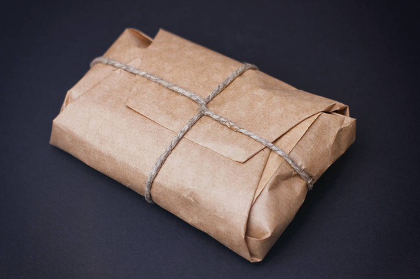 Craft wrapped package on black background. Parcel with hemp cord.  - Foto, afbeelding