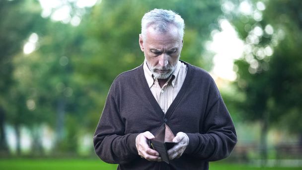 Sad pensioner holding empty wallet, retirement poverty, financial crisis, credit - Foto, afbeelding