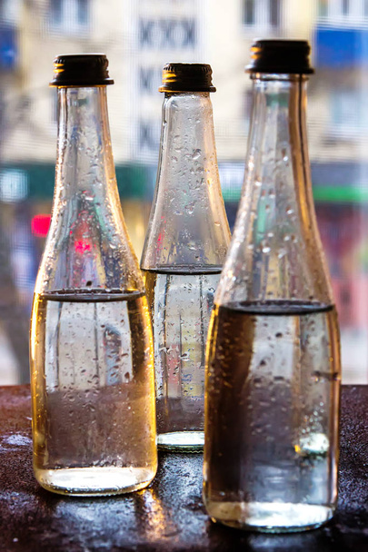 Glass bottles filled with half water in neon light on the background of the view from the window. Selective focus. - Photo, image