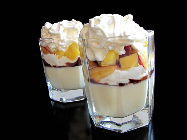 Two glasses with panna cotta dessert with peaches, whipped cream and meringue - Photo, Image