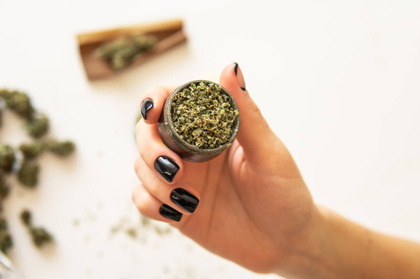 Close up of marijuana blunt with grinder. Woman rolling a cannabis blunt on white background. Woman preparing and rolling marijuana cannabis joint. marijuana use concept. Top view - Foto, Bild