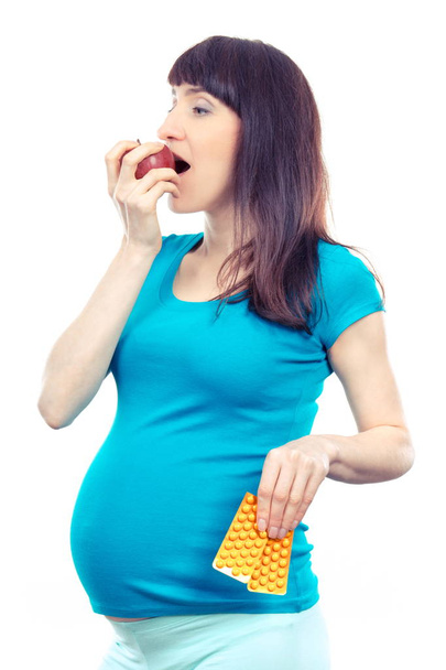 Happy pregnant woman eating apple and holding medical pills or supplements - Photo, Image