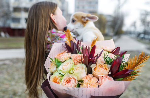 Mooie vrouw met een boeket bloemen houdt een pup in haar handen. Selectieve focus in bloemen - Foto, afbeelding